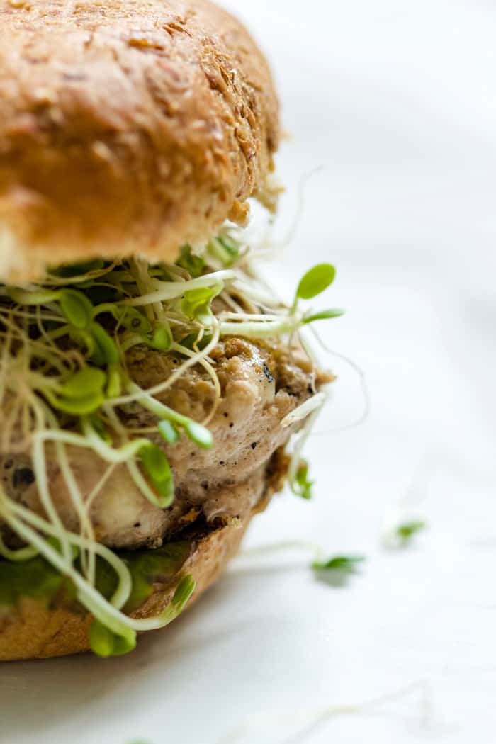 Close-up of turkey pesto walnut burger on sprouted grains roll with sprouts, lettuce, and avocado