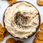 Everything bagel seasoning hummus on wooden plate with sweet potato chips