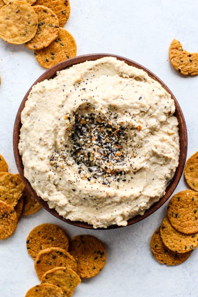 Everything bagel seasoning hummus on wooden plate with sweet potato chips