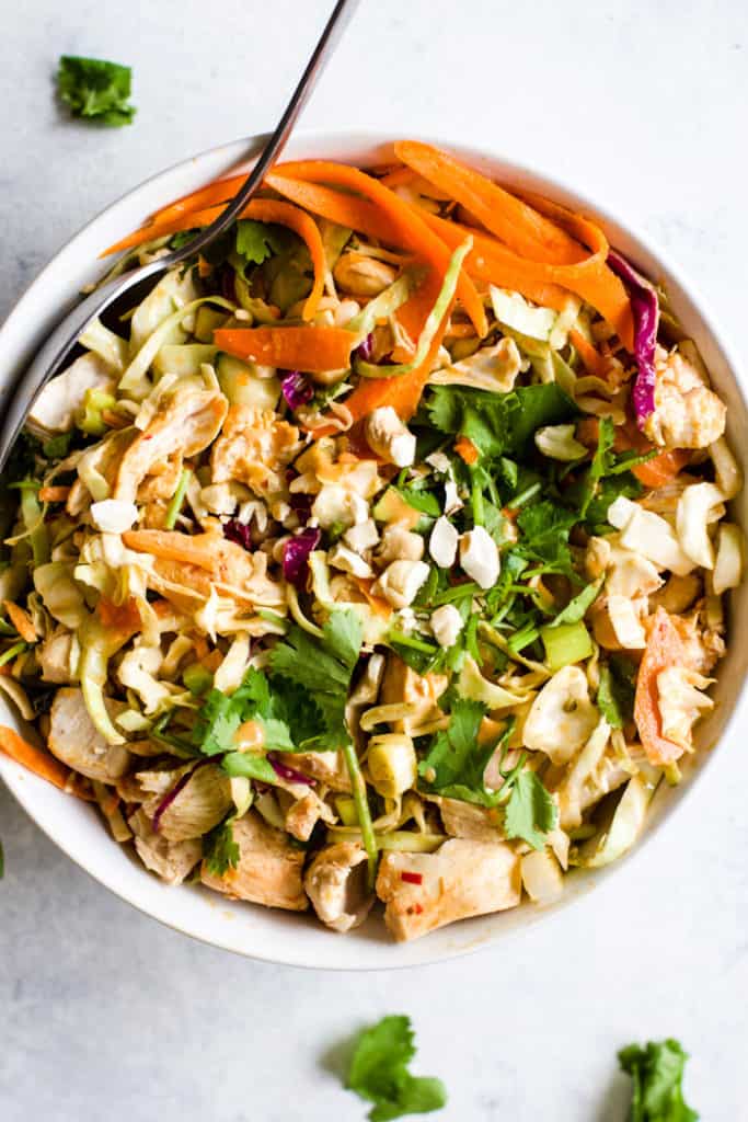 Thai peanut chicken salad with spicy peanut dressing in white bowl with spoon