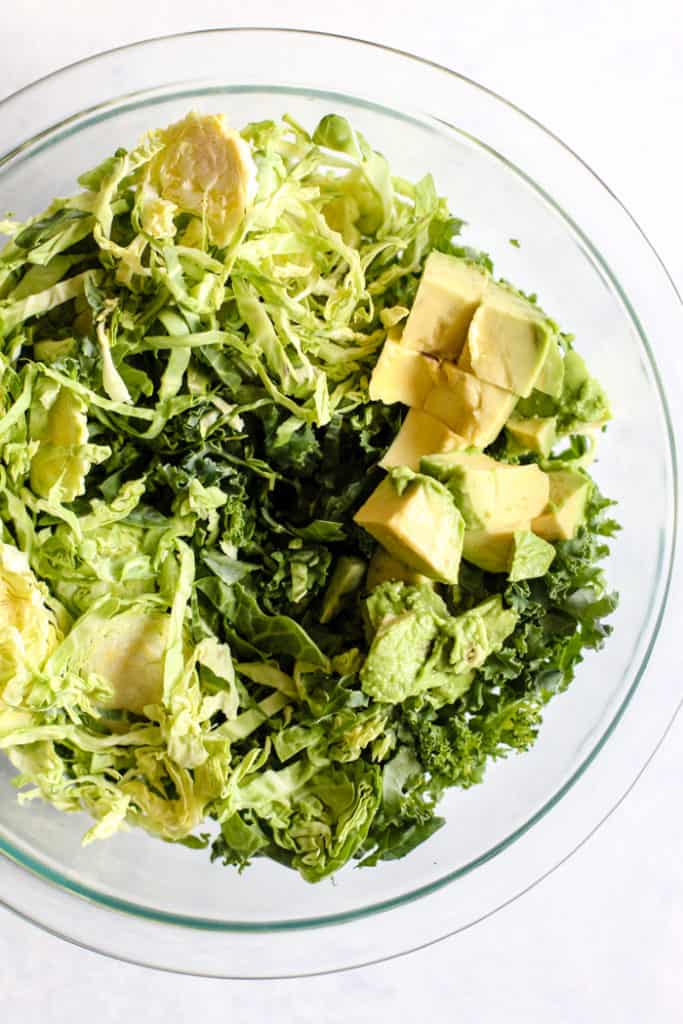 Shredded kale and Brussels sprouts with diced avocado in clear bowl