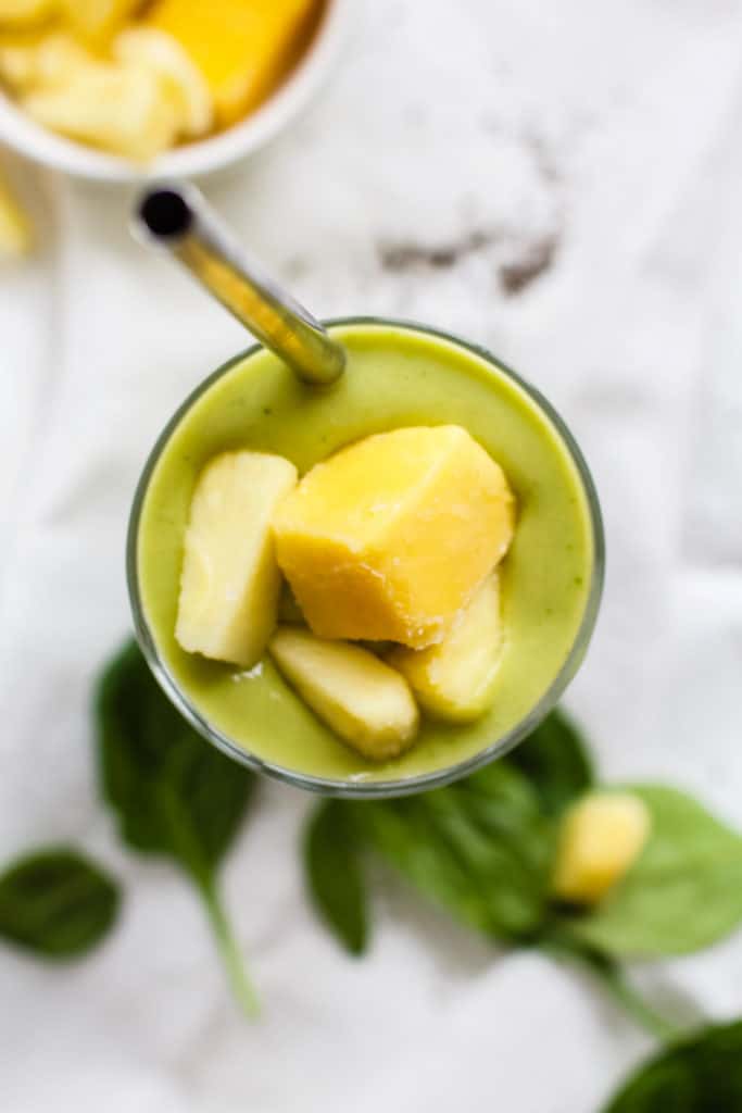 Pineapple mango avocado smoothie in tall glass with steel straw