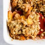Baked healthy cinnamon peach crisp in white ceramic baking dish with red spatula