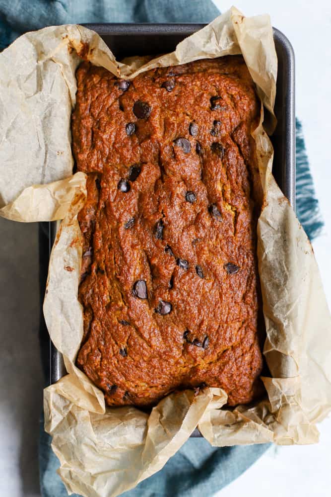 Healthy pumpkin chocolate chip bread fresh out of the oven in parchment-lined loaf pan