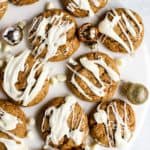 Flourless almond butter cookies, drizzled with white chocolate, on white marble surface with a few small ornaments and white chocolate chips sprinkled around