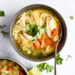 Ginger lime chickek noodle soup in dark gray bowl garnished with cilantro, on light blue surface