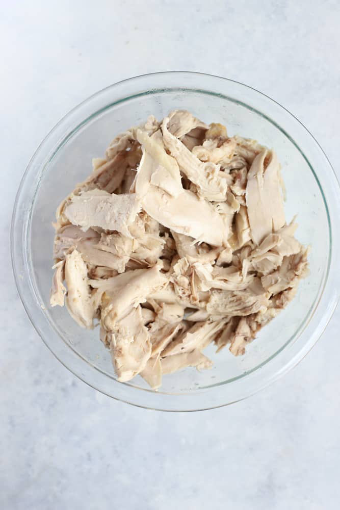 Shredded cooked chicken in clear glass bowl on light blue surface