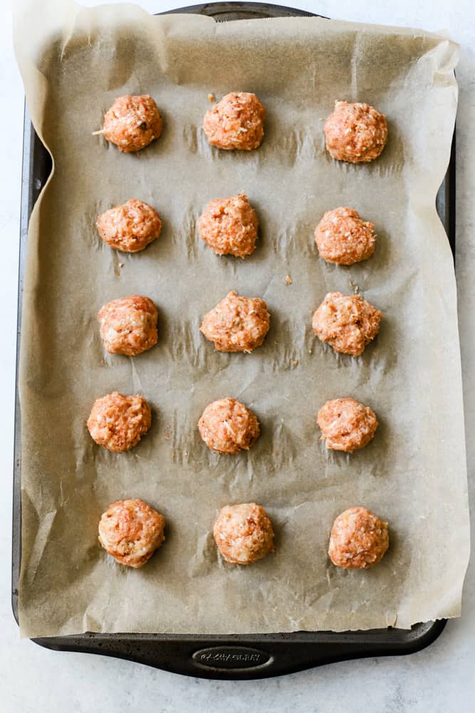 Raw Spanish baked chicken meatballs on parchment on sheet pan before baking