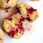 One wholesome raspberry lemon muffin cut open on white marble cake stand, with tender inner crumb and juicy raspberries showing