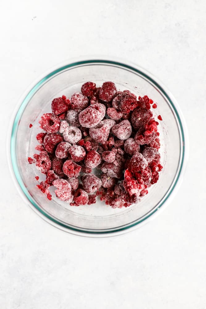 Raspberries in a clear glass bowl, tossed in a little white whole wheat flour
