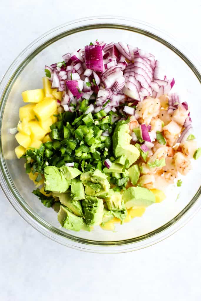 Zesty shrimp mango and avocado salad ingredients in clear glass bowl before being mixed