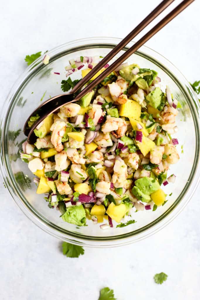 Zesty shrimp mango and avocado salad in clear glass bowl with copper serving spoons