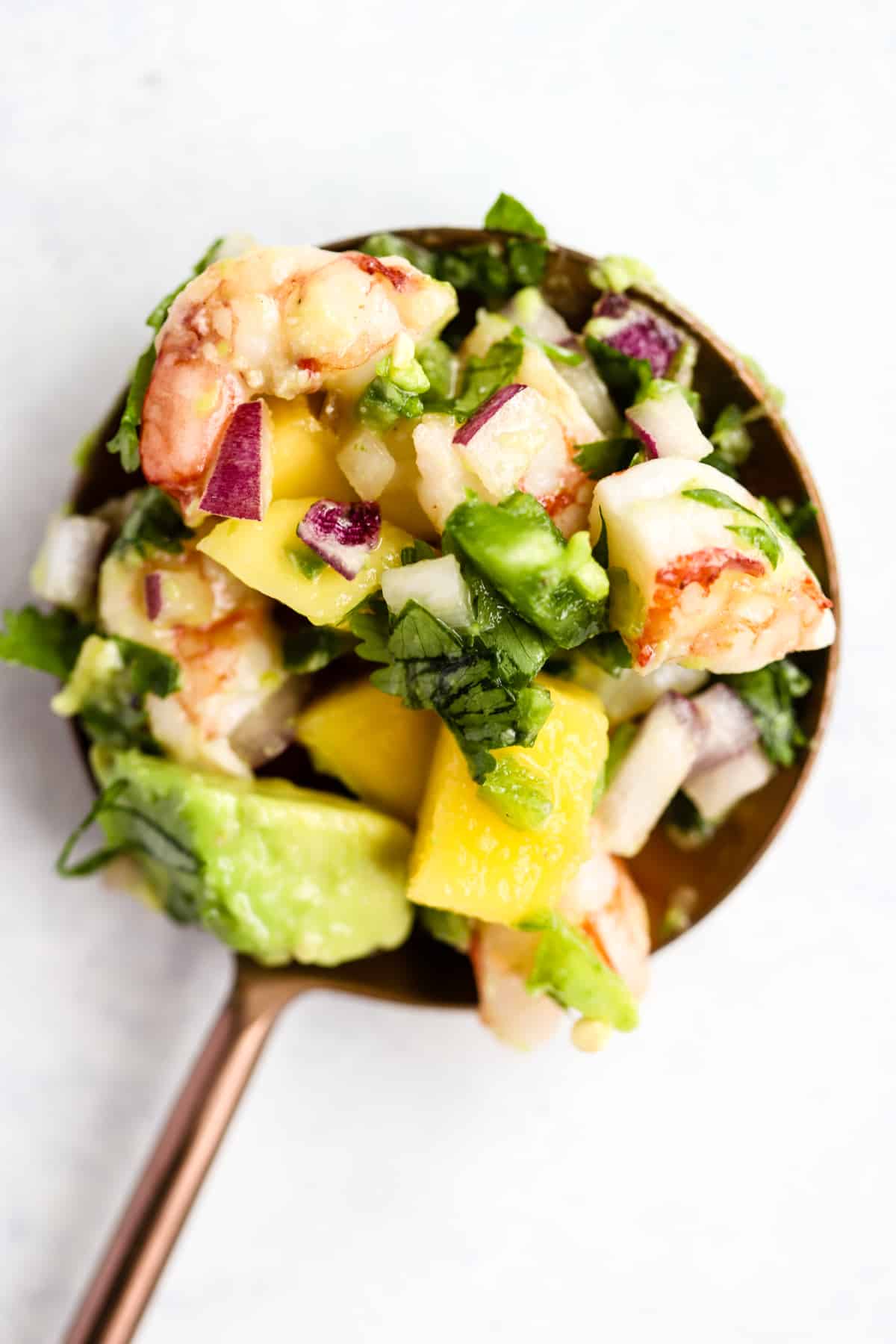 Zesty shrimp mango and avocado salad scooped into copper serving spoon