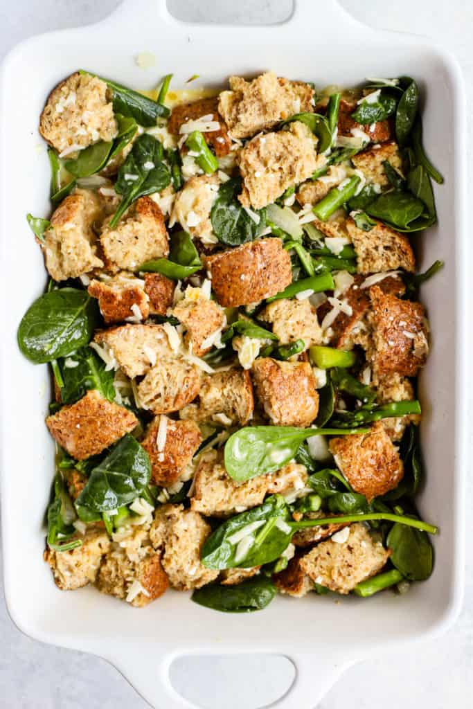 Whole grain bread cubes, asparagus pieces, and diced onion in white baking dish