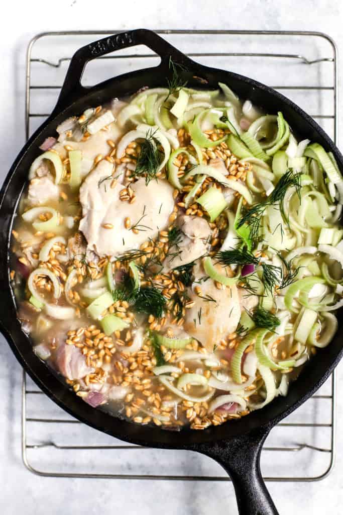 Browned chicken thighs, leeks, onions, garlic, dill, and uncooked farro in skillet with water, right before cooking in oven