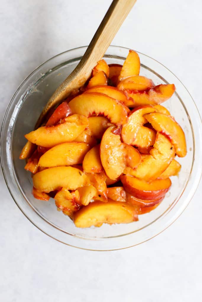 Peach crisp filling in clear glass bowl with wooden spoon