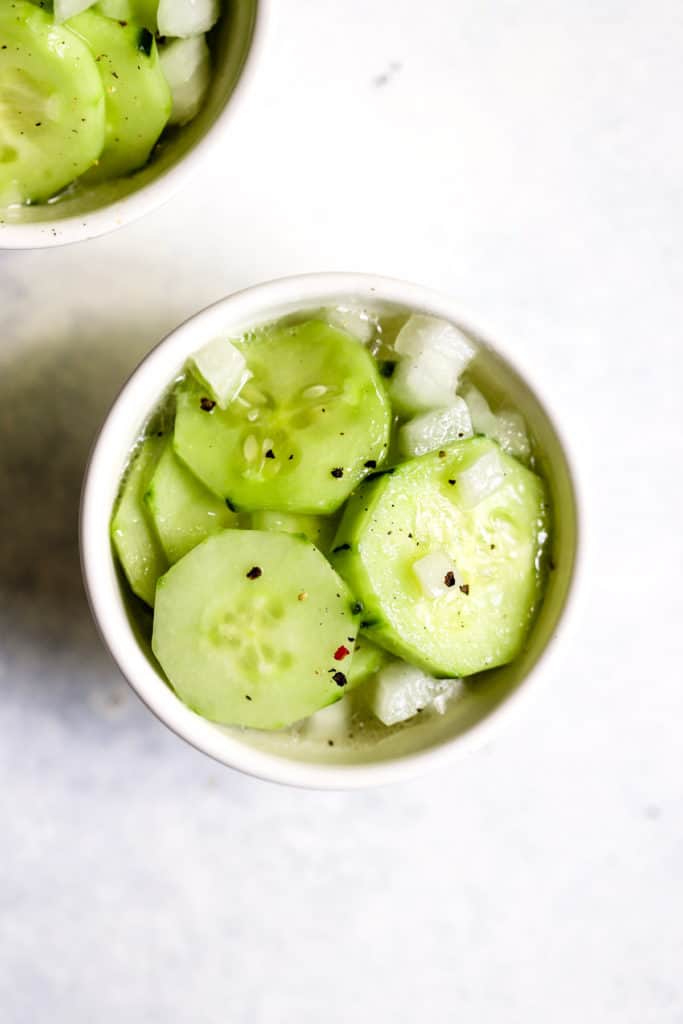 Vinegar cucumber salad in small white bowl with freshly cracked pepper on top