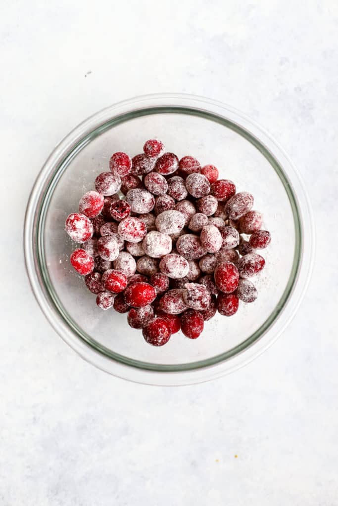 Whole fresh cranberries tossed in a bit of flour, in clear glass bowl, on light blue and white surface