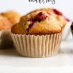 Healthy cranberry orange muffin with parchment liner on white marble cake stand, with other muffins in background