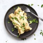 Two healthy white chicken enchiladas on dark gray plate with cilantro and fork