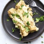 Two healthy white chicken enchiladas on dark gray plate with cilantro and fork