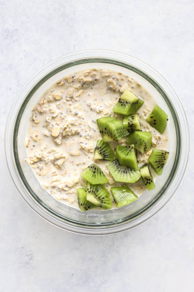 Overnight oats mixed together in clear glass bowl with kiwi sprinkled on top