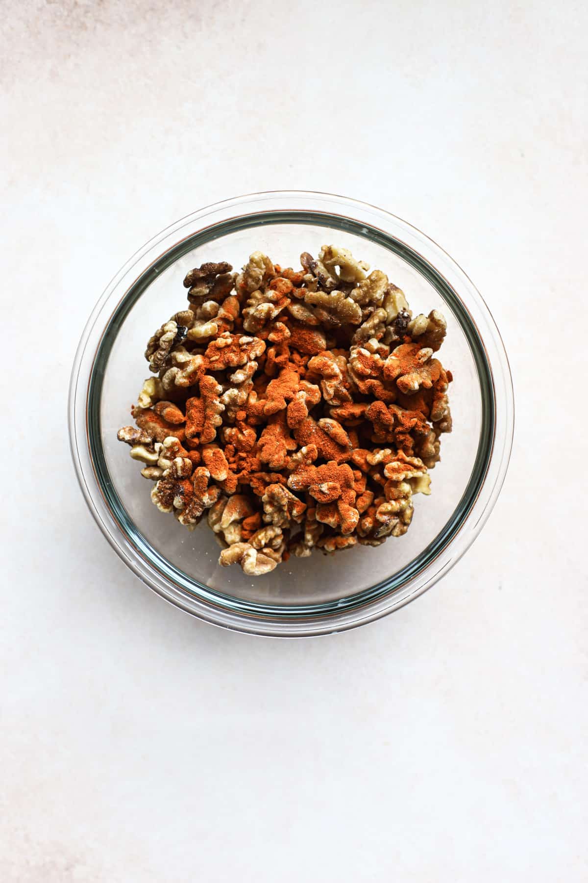 Walnuts, cayenne, and salt tossed together in clear glass bowl