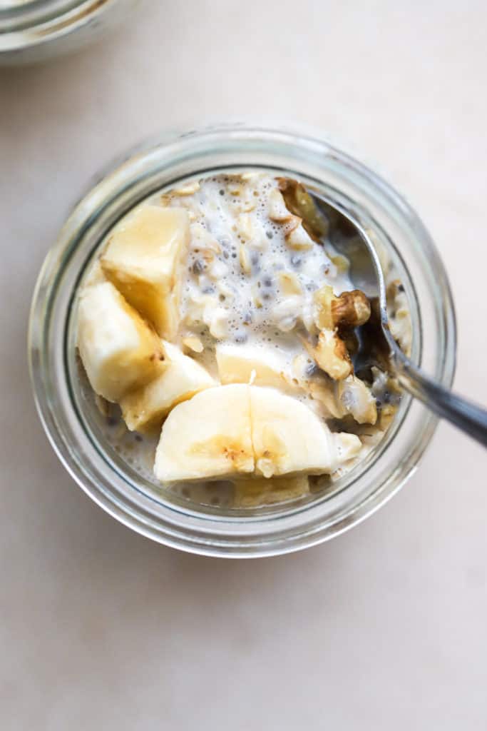 Protein overnight oats in small glass tulip jar with spoon dipped in, and topped with a few banana slices and walnuts