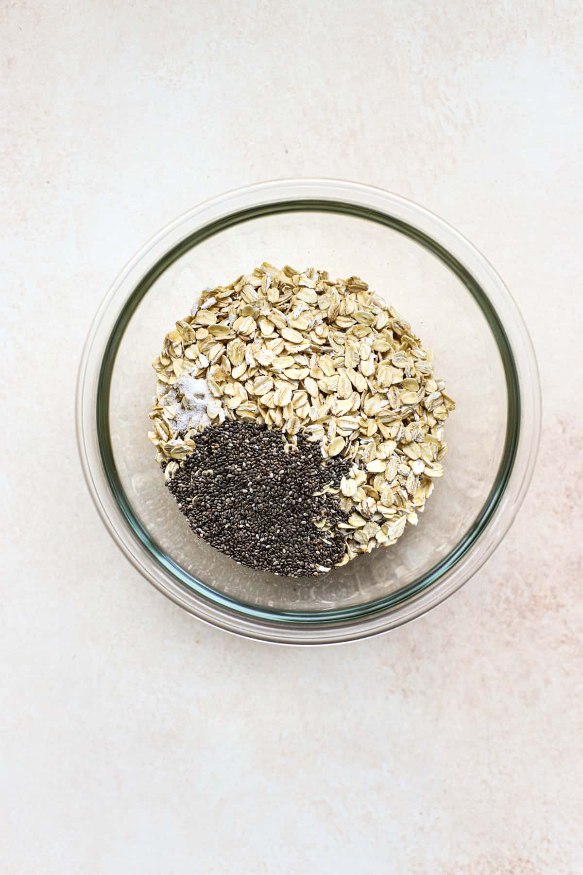 Oats, chia seeds, and salt in clear glass bowl on beige and white surface