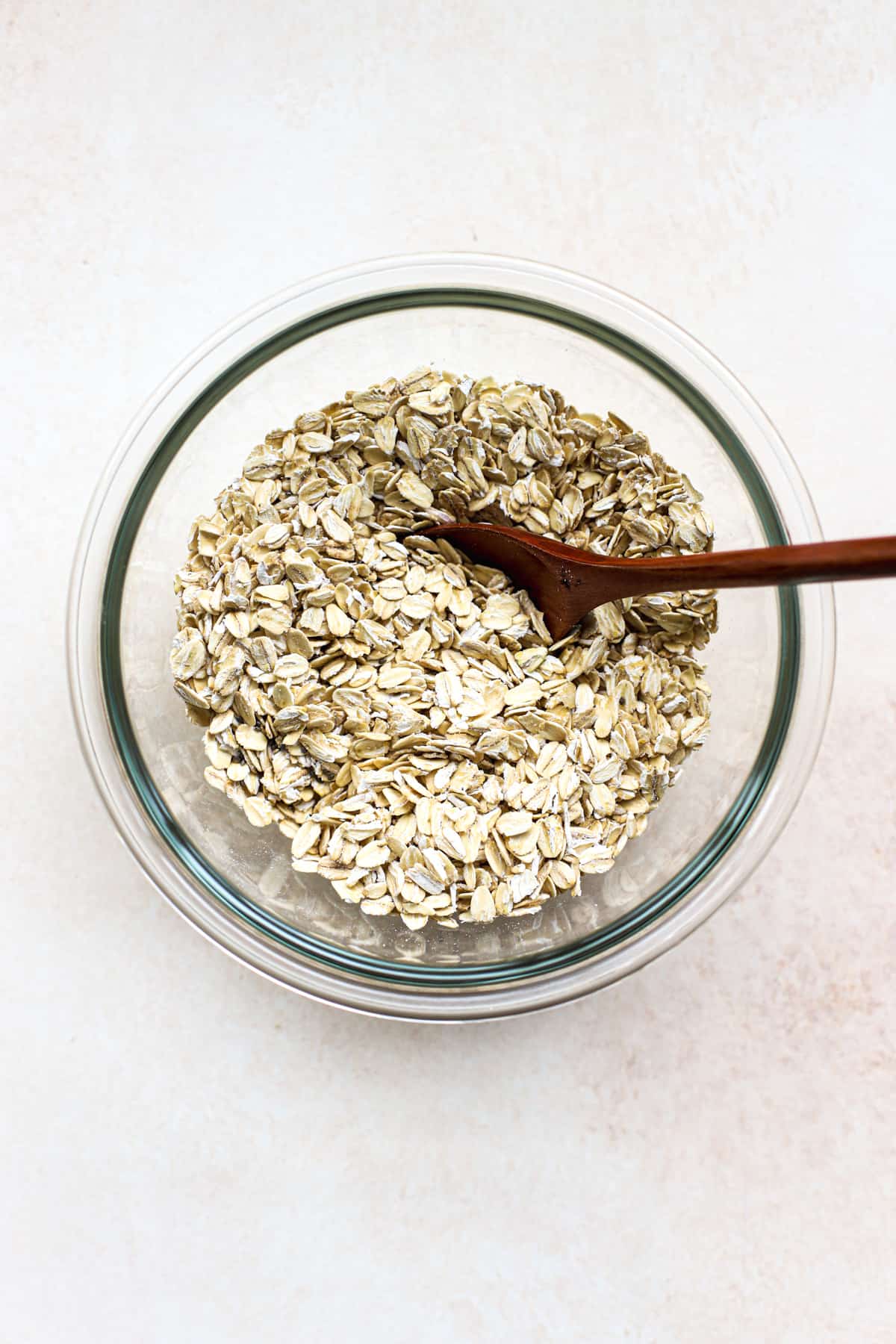 Oats, chia seeds, and salt mixed together in clear glass bowl with wooden spoon