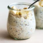 Protein overnight oats in small glass tulip jar with spoon dipped in, and topped with a few banana slices and walnuts