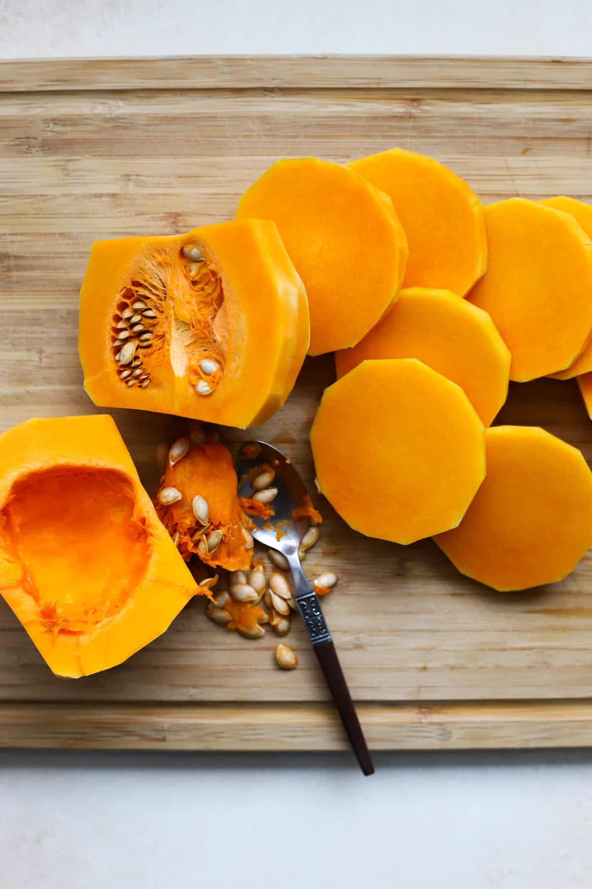 Slices of butternut squash on bamboo cutting board with spoon scooping out seeds