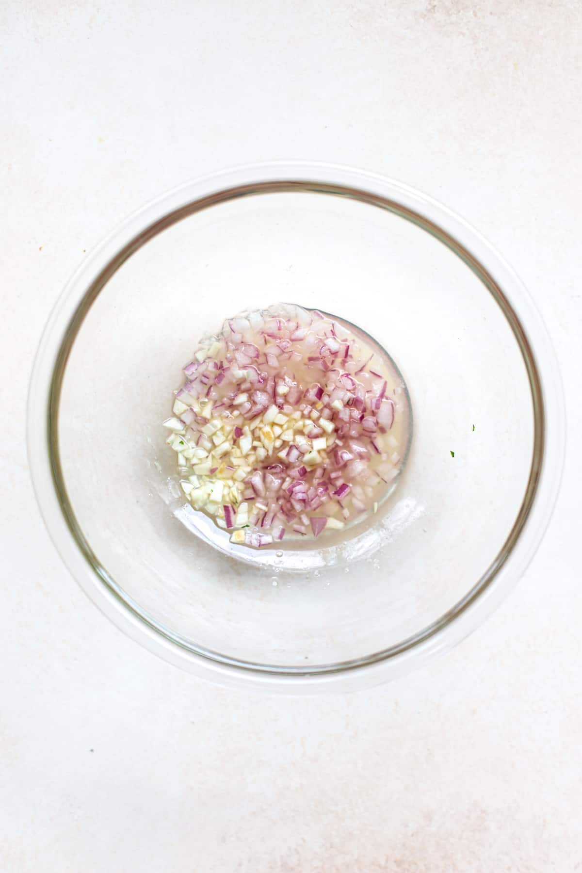 Onions and garlic macerating in lemon juice in clear glass bowl, on beige and white surface