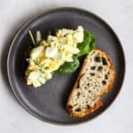 Healthy egg salad sandwich, open-faced with top slice of sourdough on the side, on dark gray plate, on light gray surface