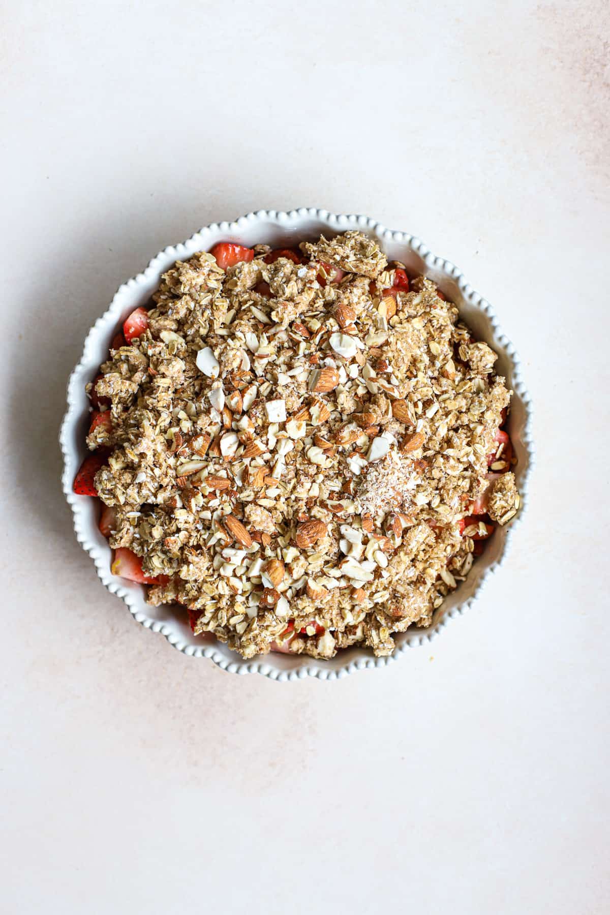 Prepared fresh strawberries in cream-colored pie dish, topped with crisp topping, before baking
