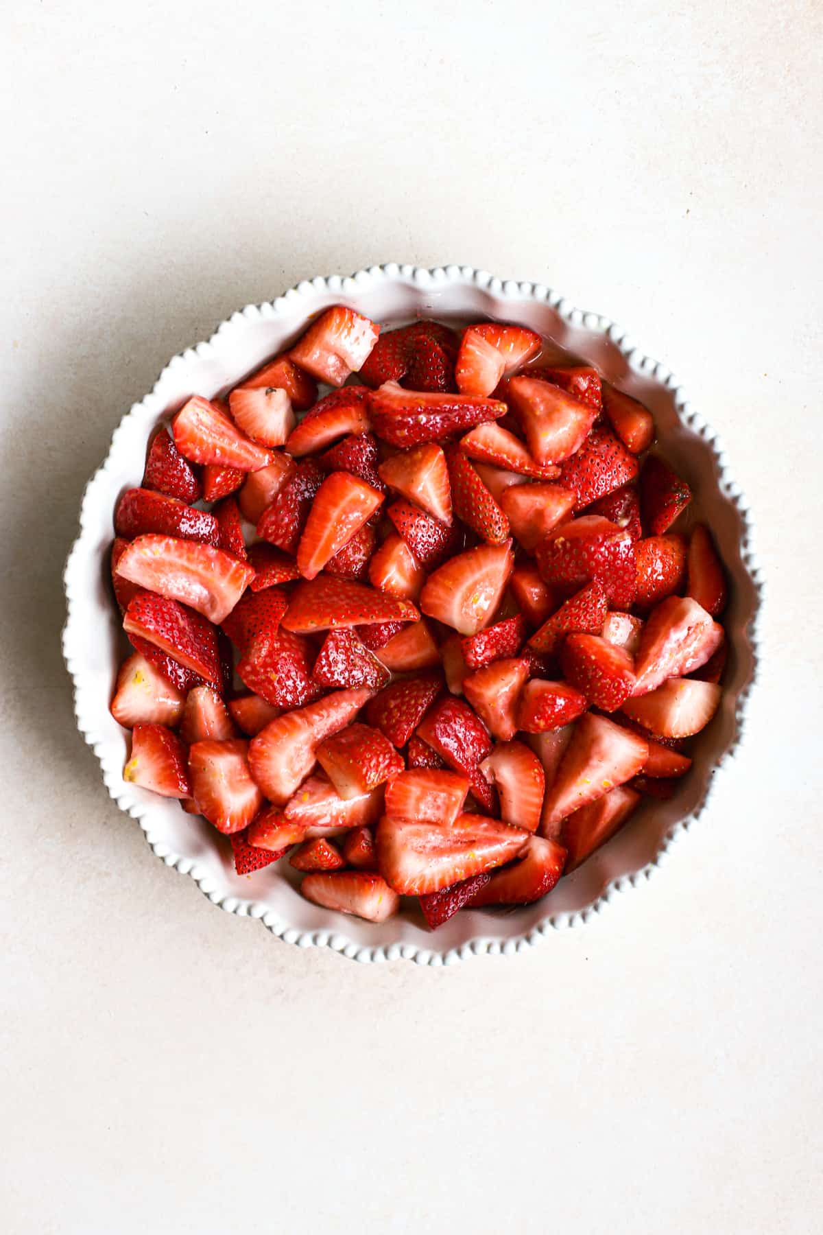 Prepared fresh strawberries in a cream-colored pie dish, on beige and white surface