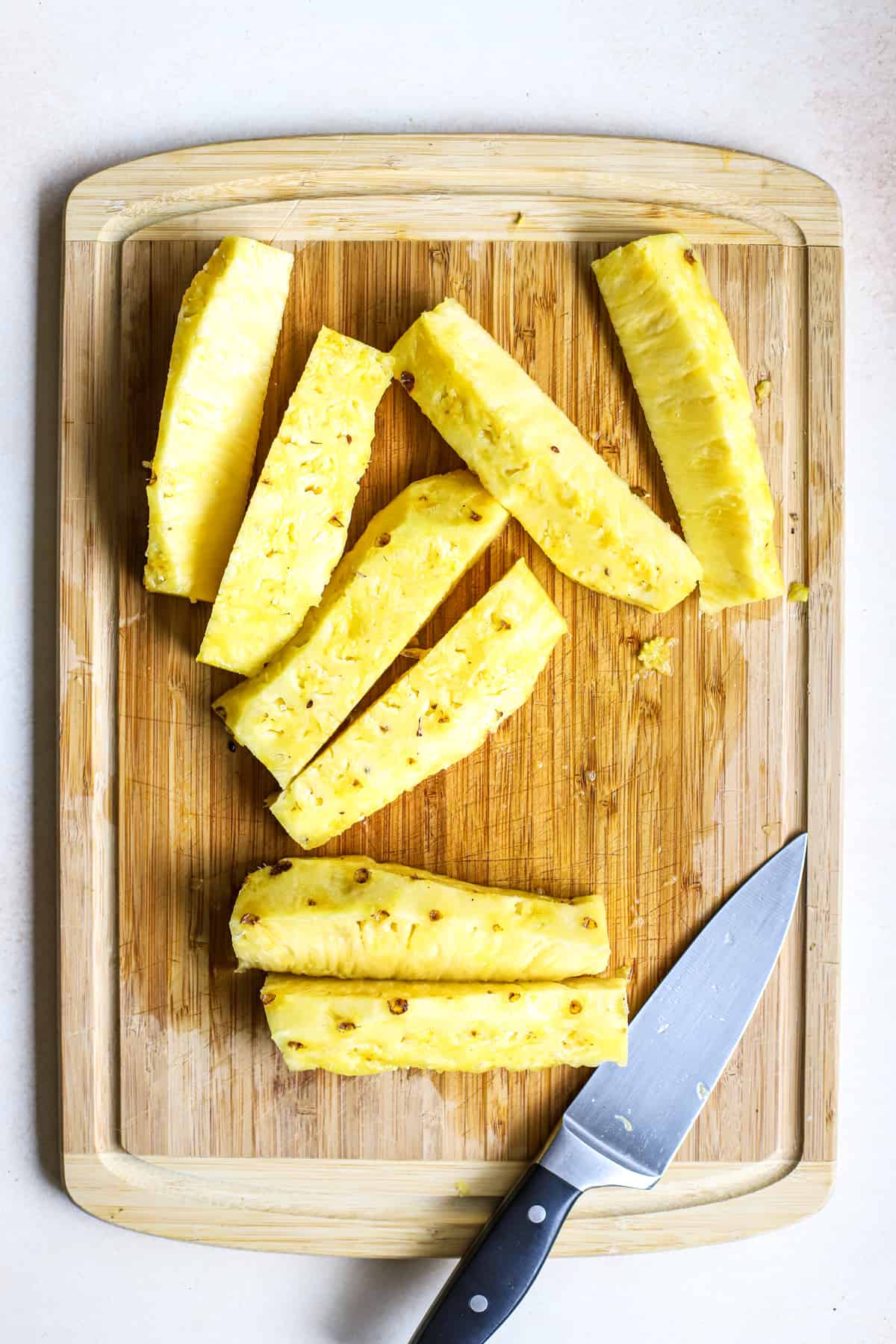 Eight long pineapple slices on bamboo cutting board next to chef's knife