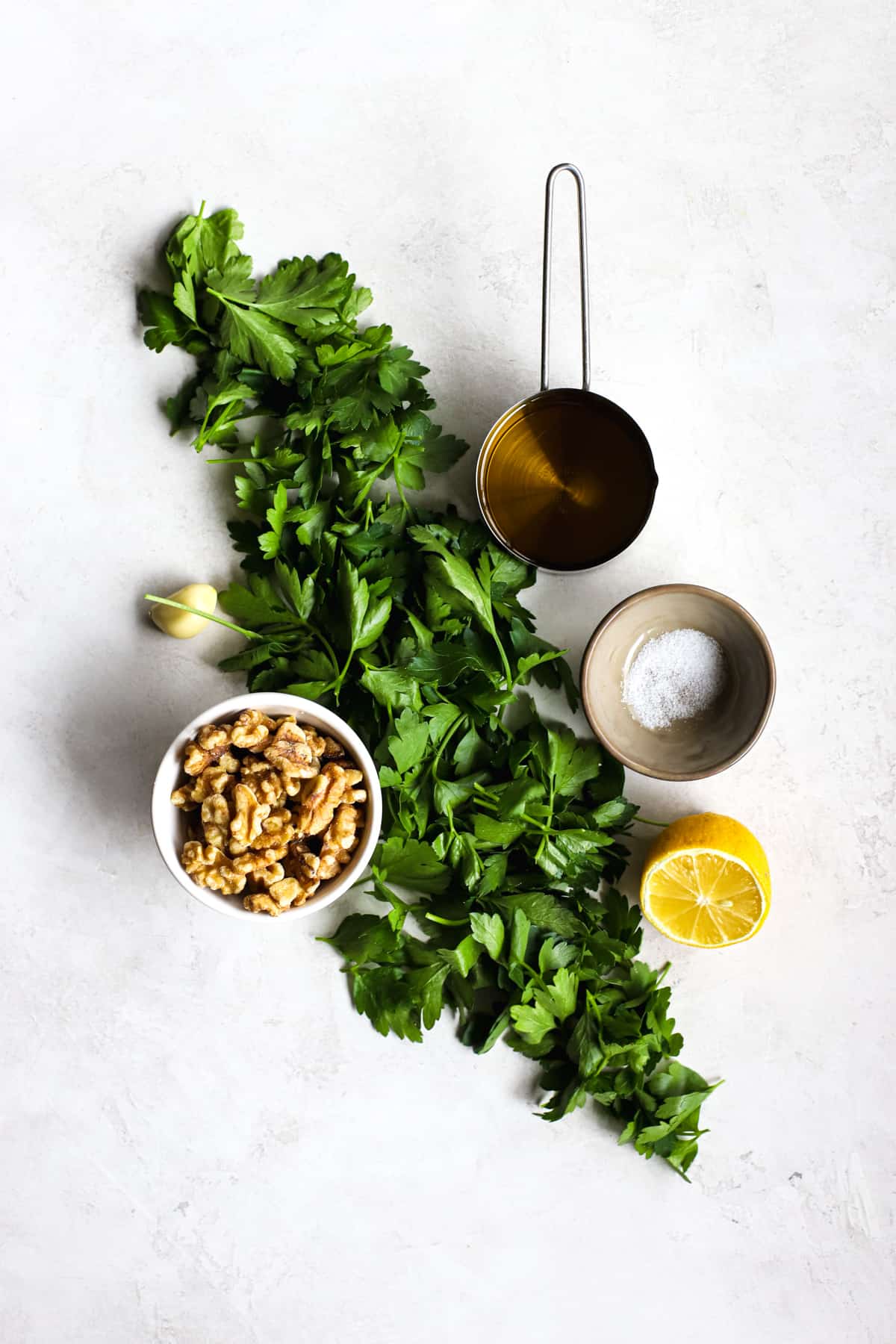 Parsley walnut pesto ingredients on light gray and white surface