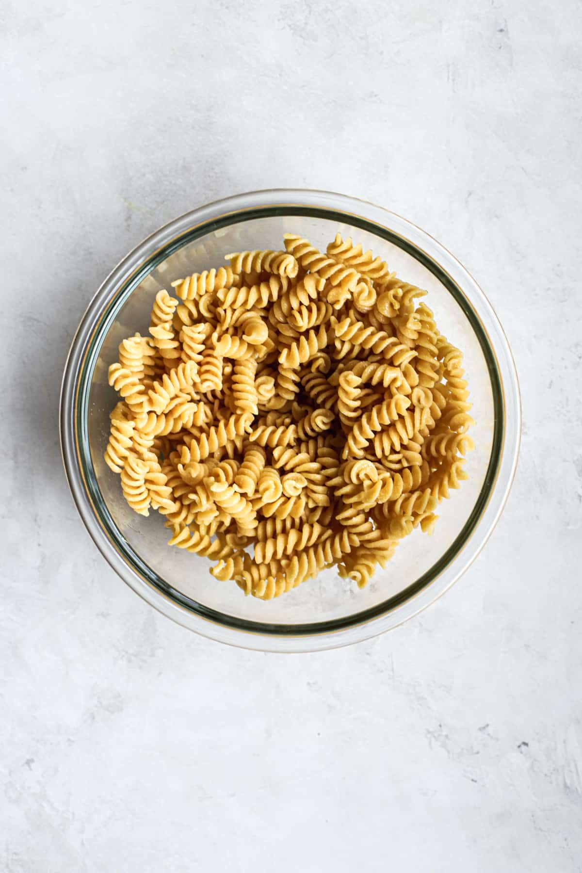 Cooked rotini in clear glass bowl on gray and white surface