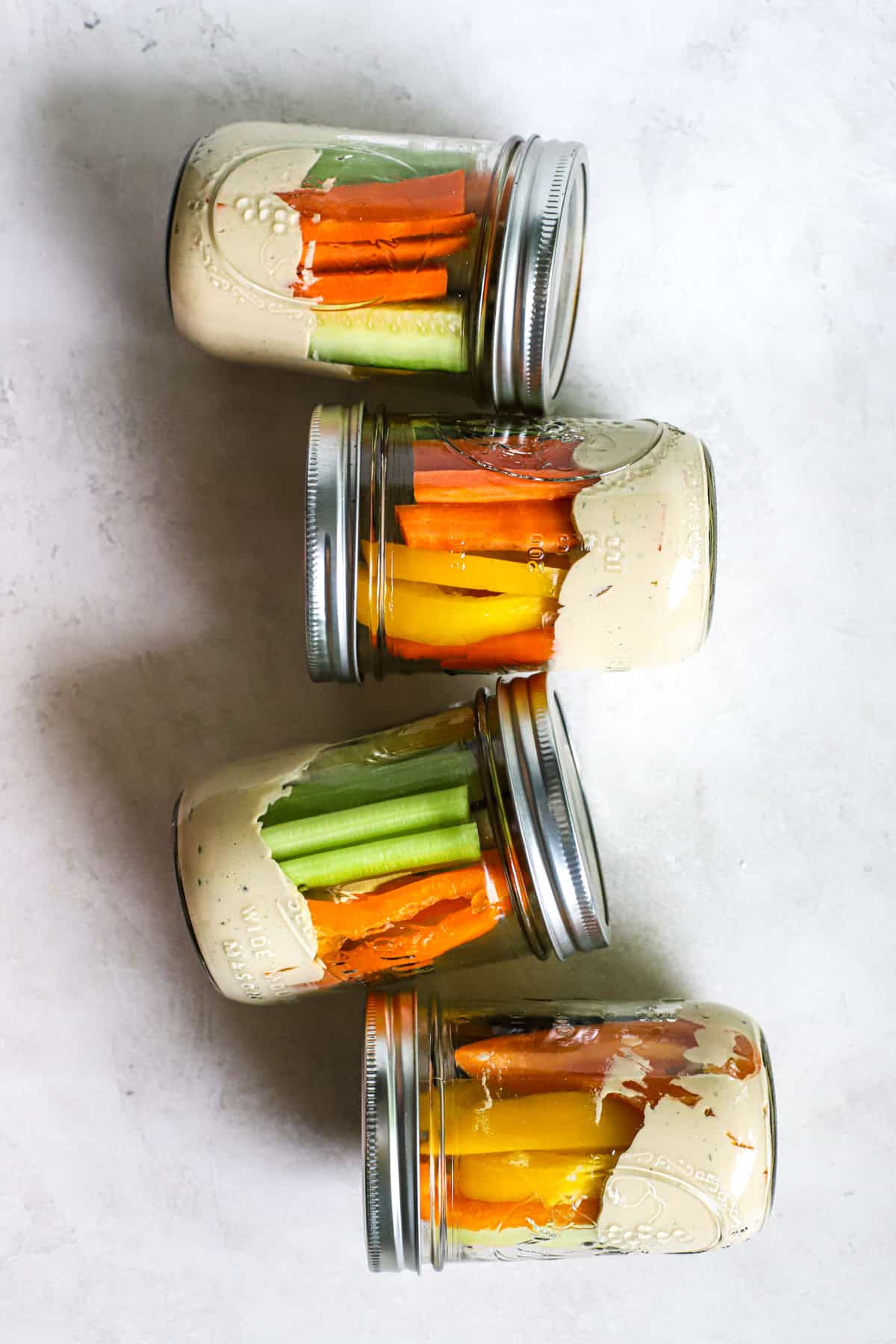 Four hummus and veggie jars lying on sides, on gray and white surface