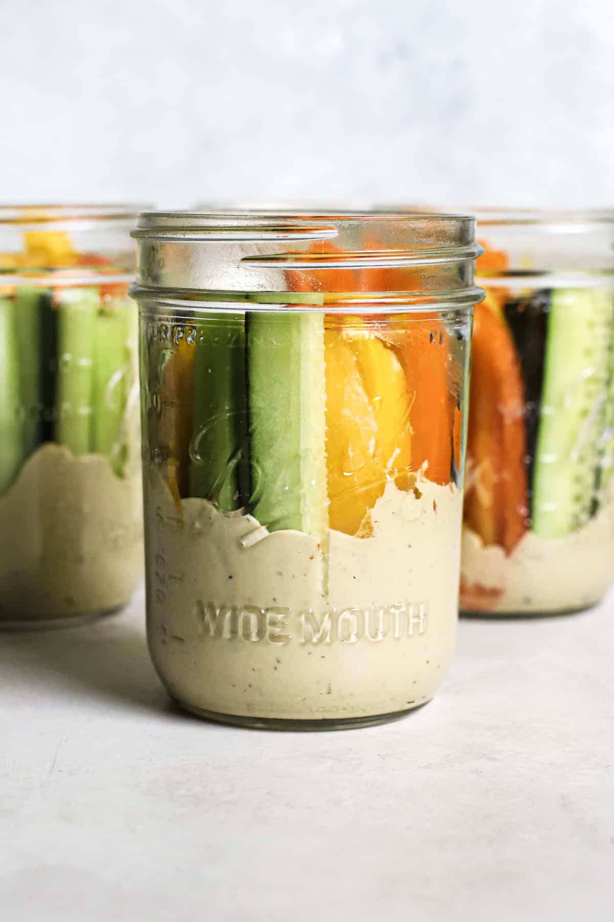 Three hummus and veggie jars on gray and white surface