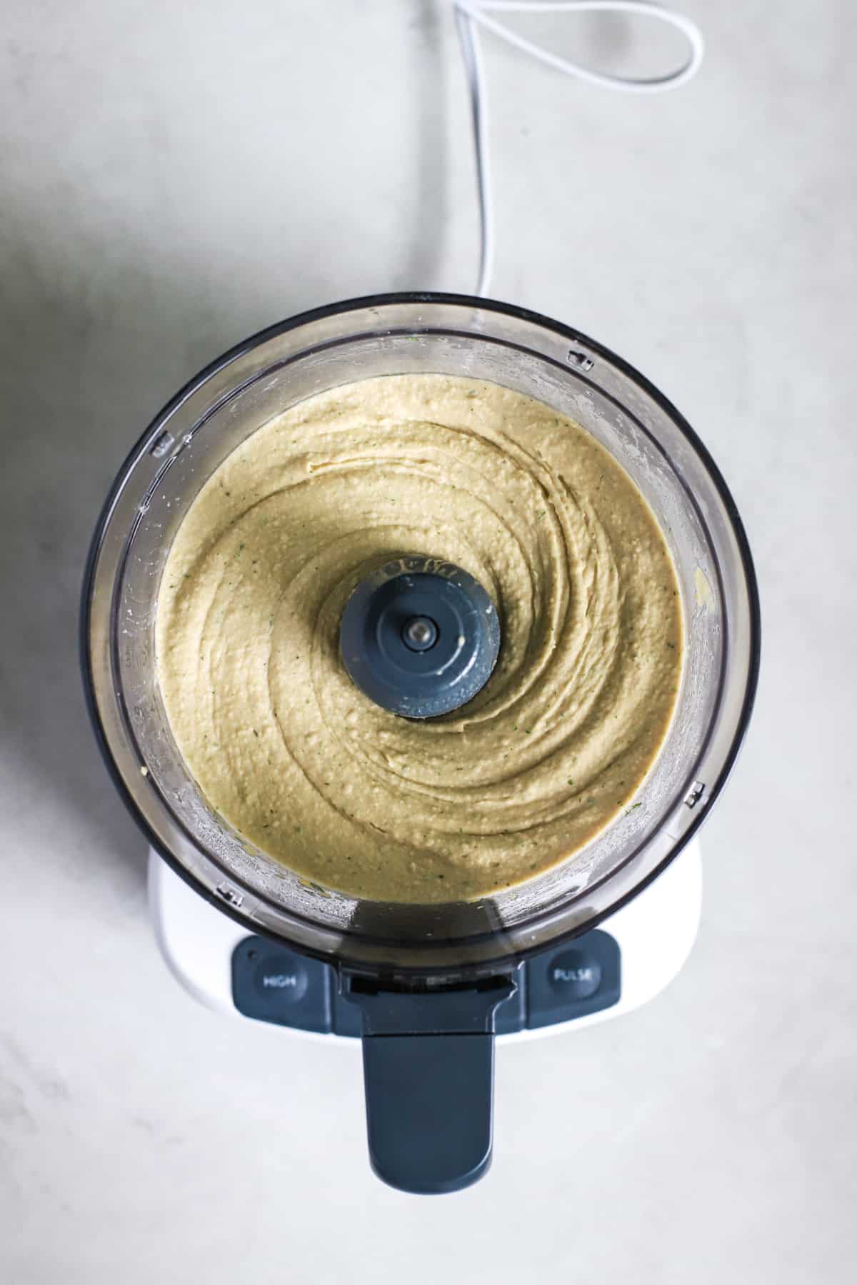 Lemon dill hummus ingredients blended together in food processor before adding ice water to smooth it out