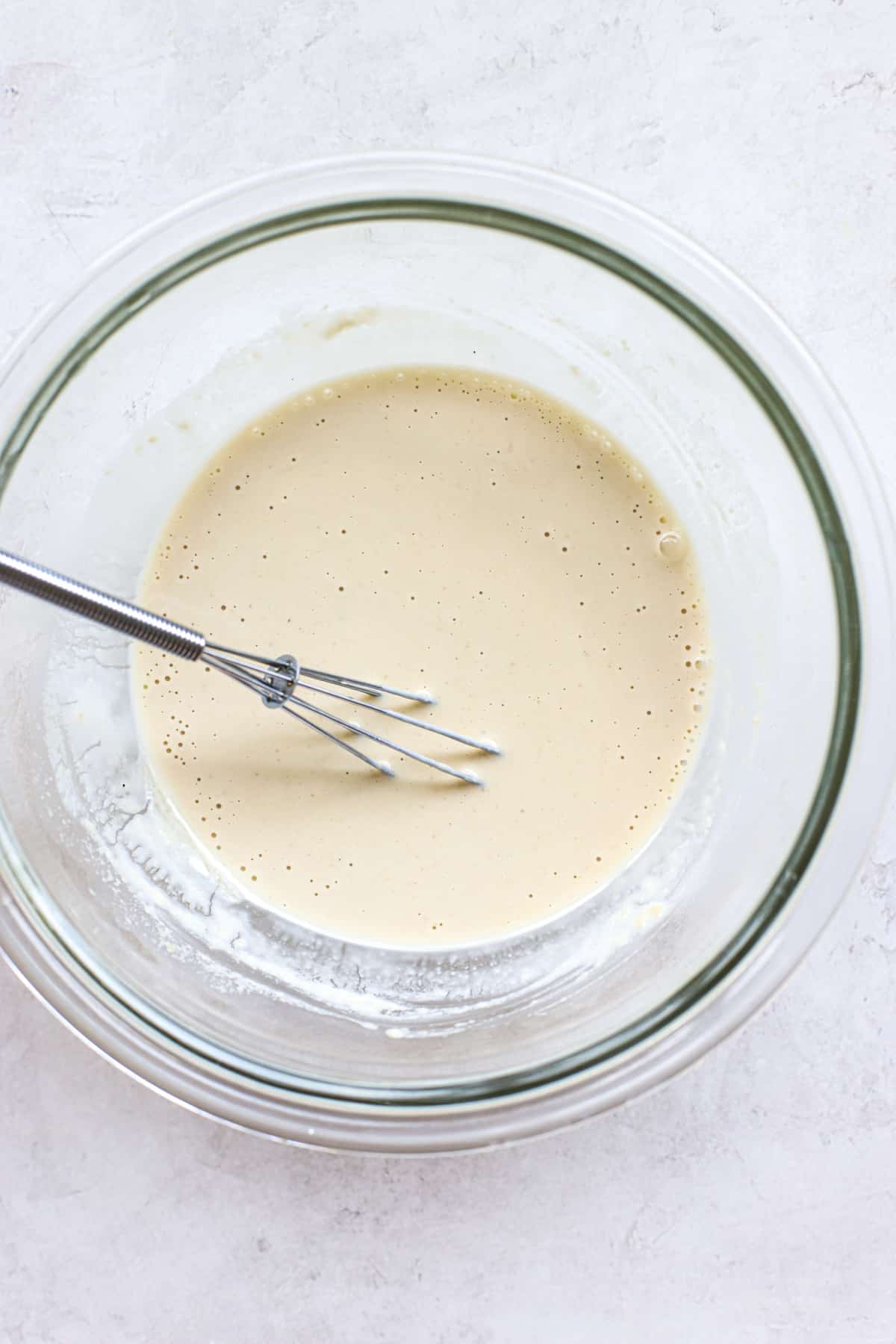 Tahini sauce completely whisked until smooth, in clear glass bowl on white and gray surface