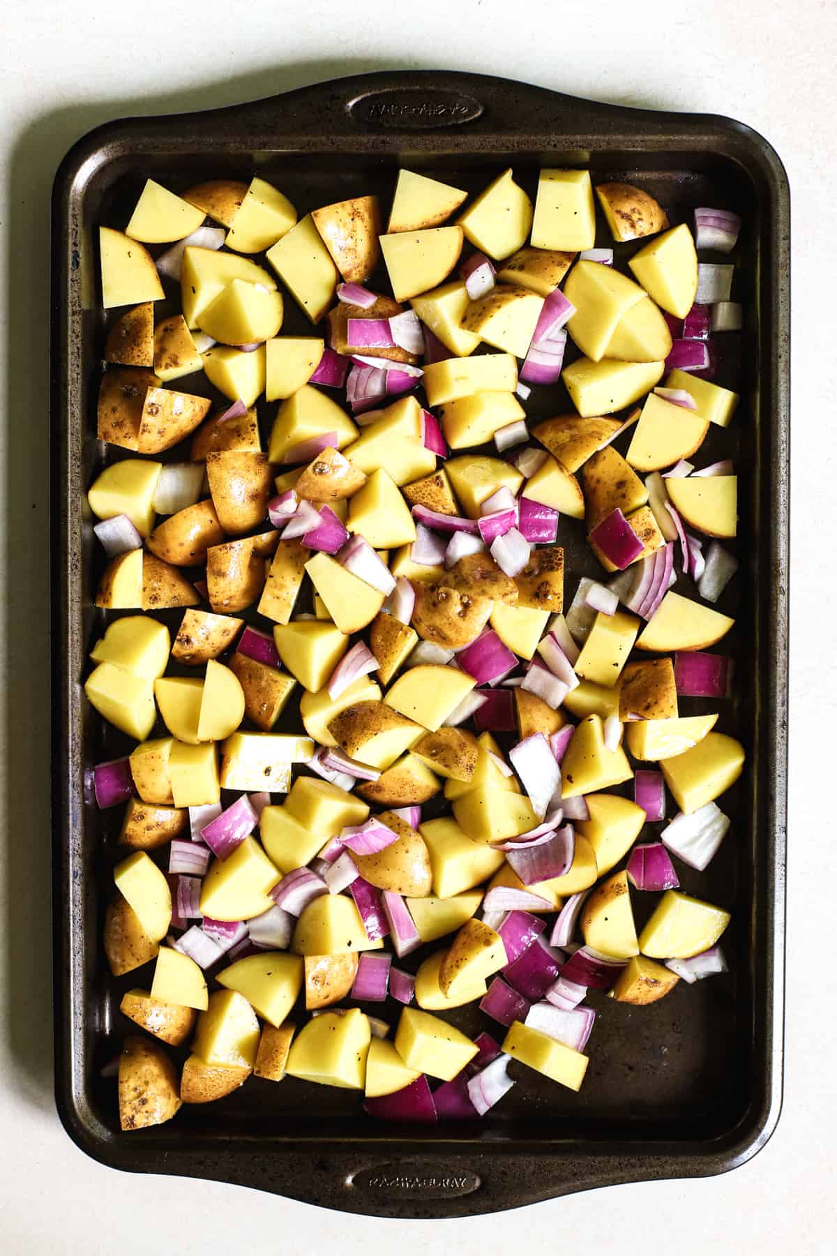 Potatoes and red onions diced large and coated in olive oil, salt, and pepper, on baking sheet