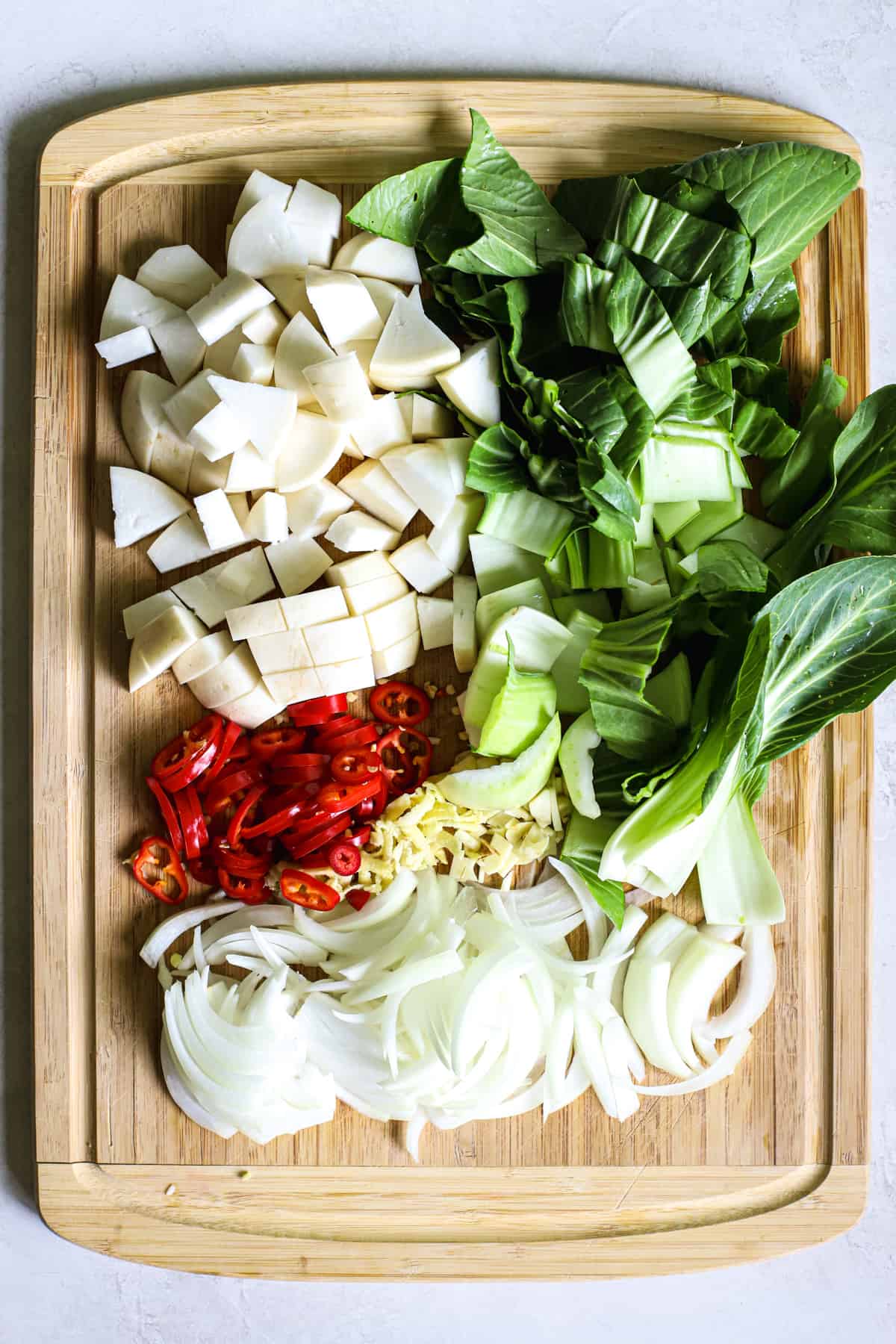 Chopped turnips, baby bok choy, red chili peppers, garlic, ginger, and sliced onions on bamboo cutting board