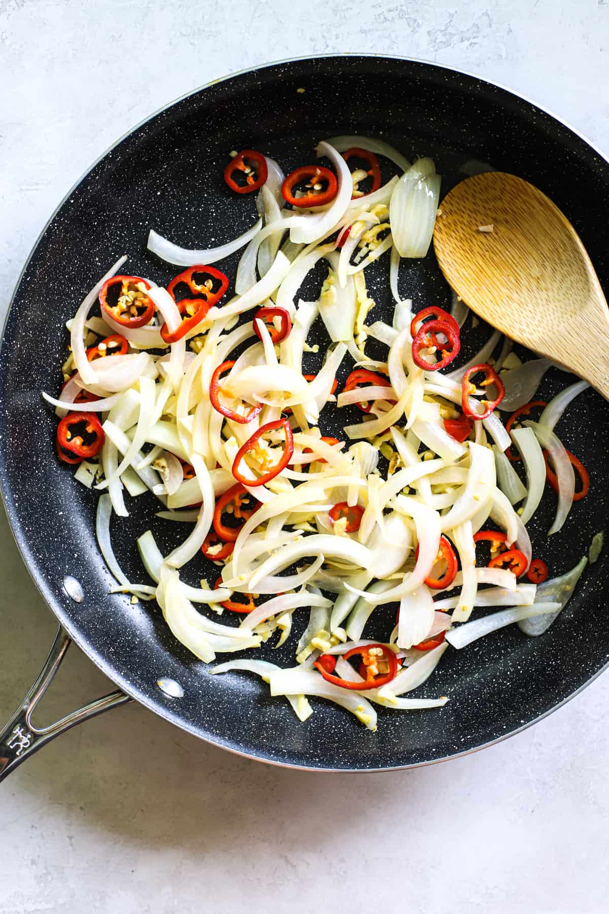 Sliced onions, chili peppers, garlic, and ginger being sautéed in coconut oil