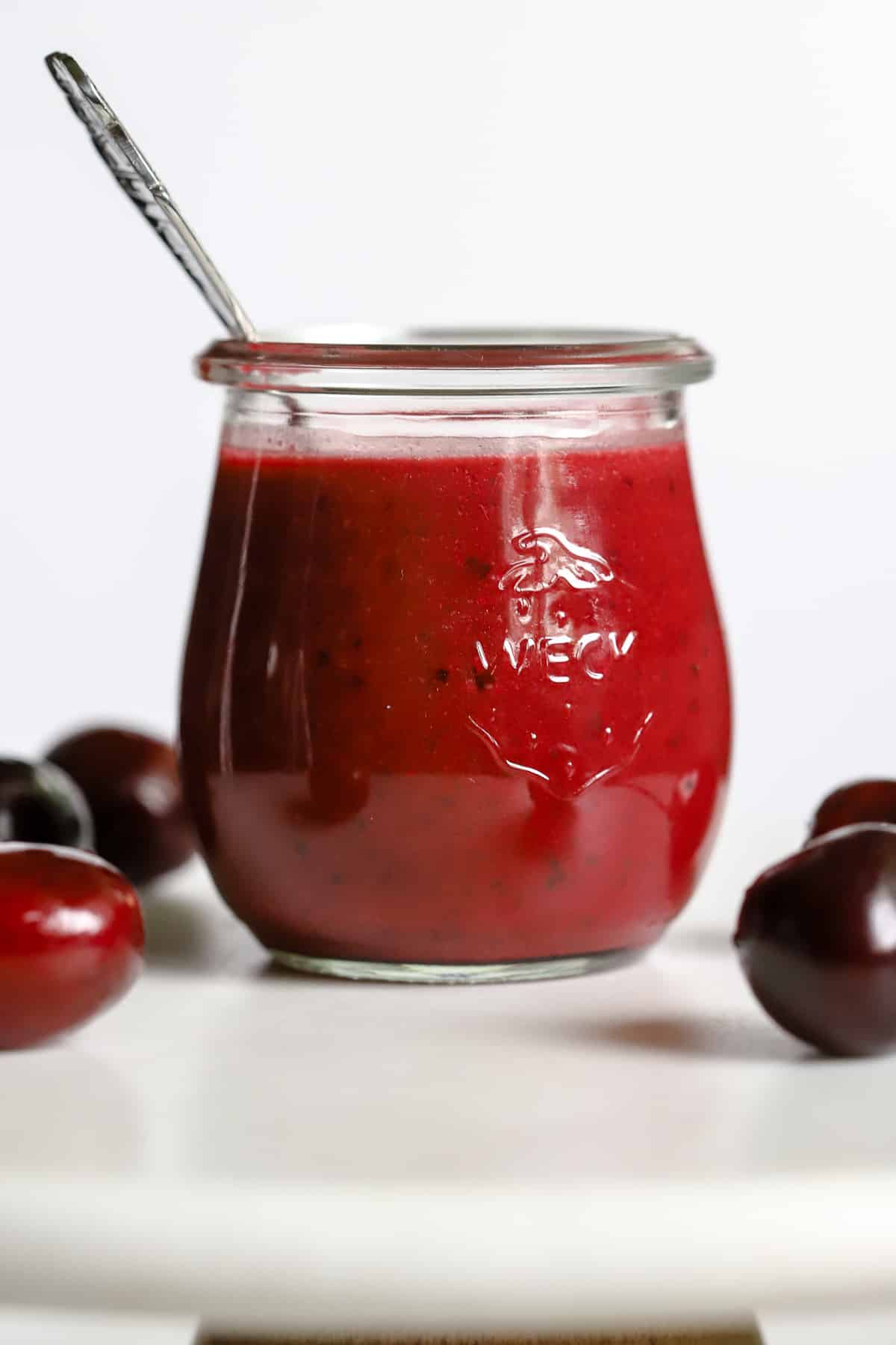 Cherry vinaigrette in small glass jar with spoon, on white marble stand with a few cherries
