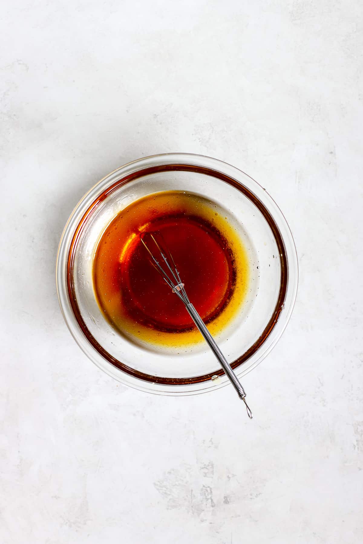 Maple syrup, coconut oil, and vanilla whisked together in small glass bowl on gray/white surface