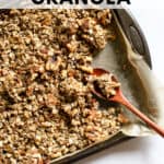 Maple cinnamon walnut granola fully baked, on parchment-lined sheet pan with wooden spoon, and a few clusters broken up