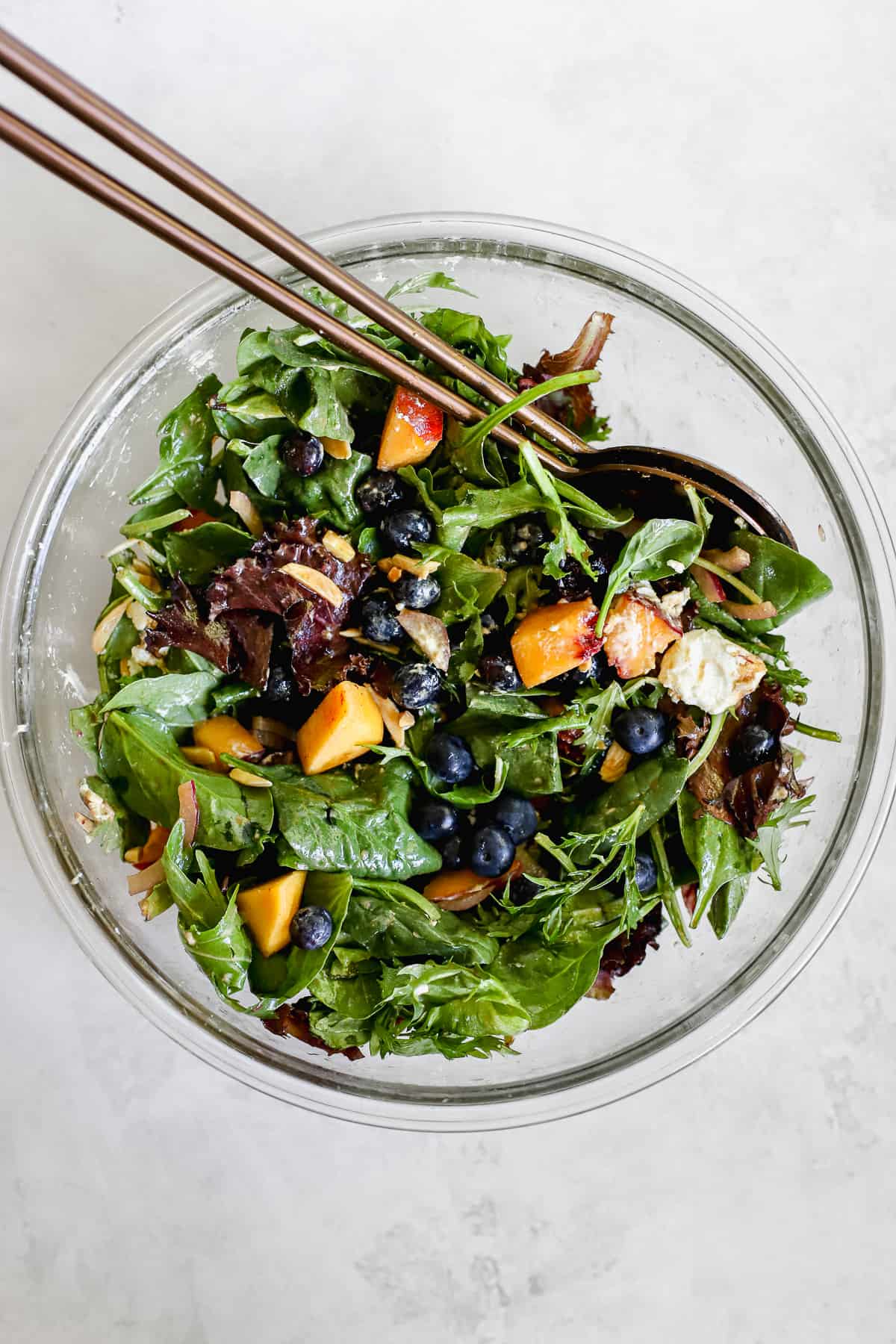 Peach blueberry salad tossed in clear glass bowl with salad copper salad tossing spoons